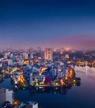 Hanoi cityscape at twilight with illuminated buildings reflecting in Hoan Kiem Lake waters