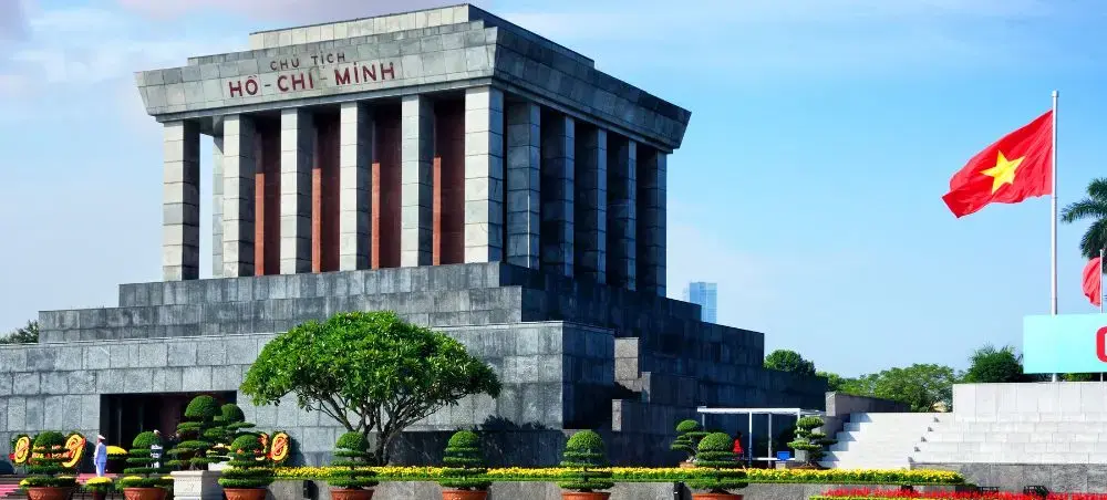 Ho Chi Minh Mausoleum in Hanoi with Vietnamese flag, iconic granite monument and presidential palace