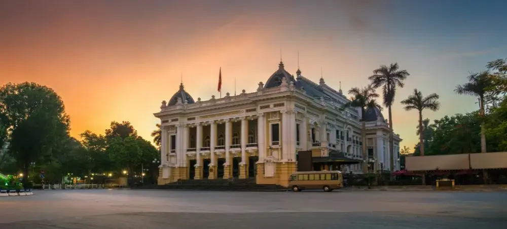 Hanoi Opera House illuminated at sunset with French colonial architecture and palm trees in Vietnam