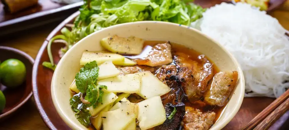 Traditional Vietnamese pho soup with beef and herbs served alongside rice noodles in Hanoi restaurant