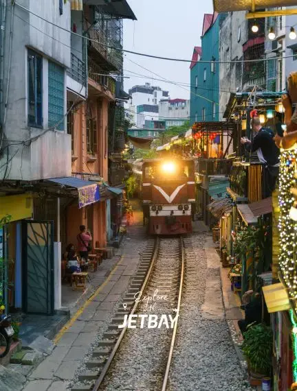 Train traveling through narrow residential street lined with colorful houses in Hanoi's famous railway quarter