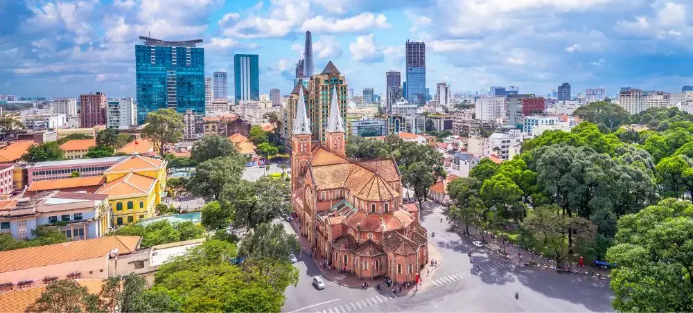 Aerial view of Ho Chi Minh City showcasing Notre Dame Cathedral amid modern skyscrapers and lush greenery