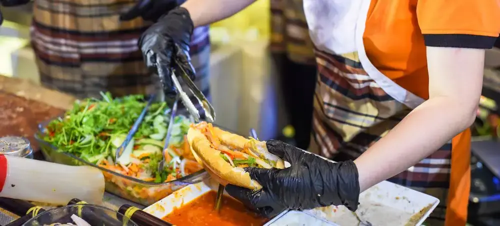 Street food vendor preparing fresh banh mi sandwich with herbs and vegetables in Ho Chi Minh City market