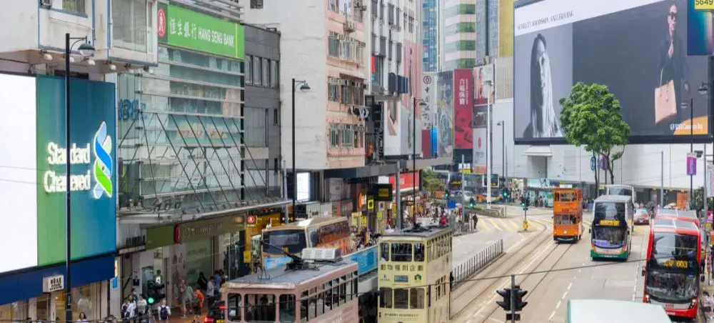 Bustling Hong Kong street scene with iconic double-decker trams, colorful signage and urban skyline