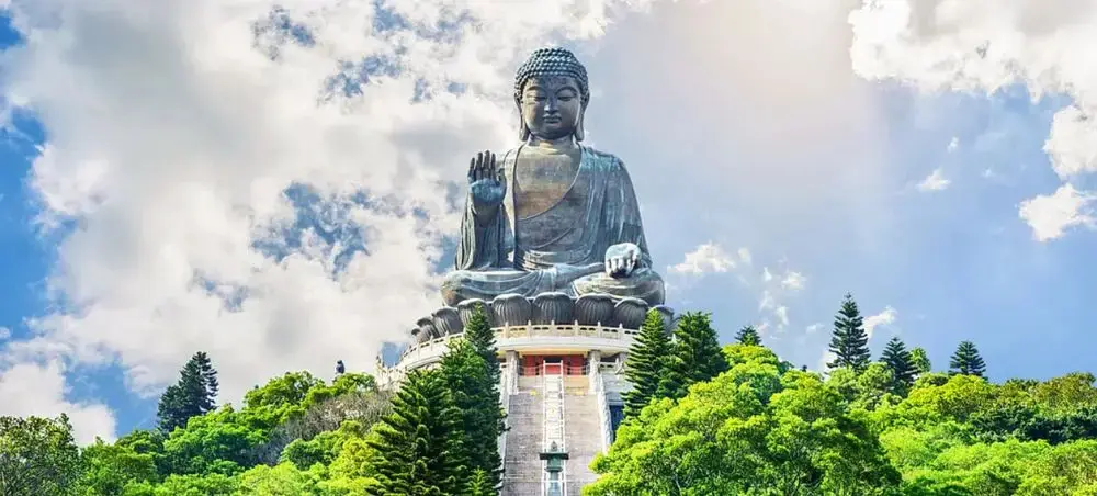Majestic Tian Tan Buddha statue surrounded by lush green mountains under dramatic cloudy skies in Hong Kong