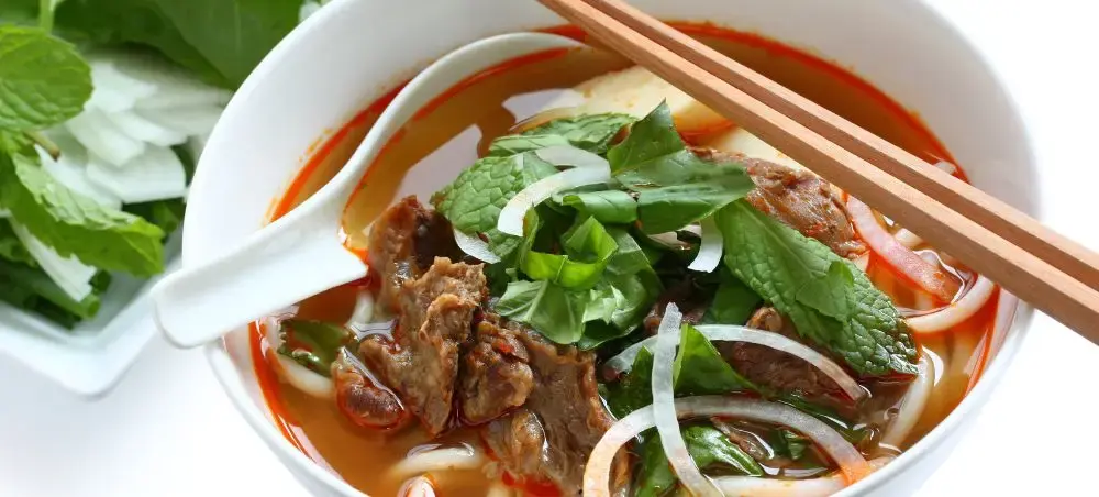 Traditional Vietnamese beef noodle soup with fresh herbs and chopsticks showcasing Hue's authentic cuisine