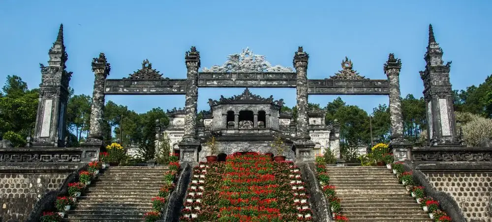 Ornate stone gateway and stairs leading to Khai Dinh Tomb in Hue, Vietnam with colorful flower displays