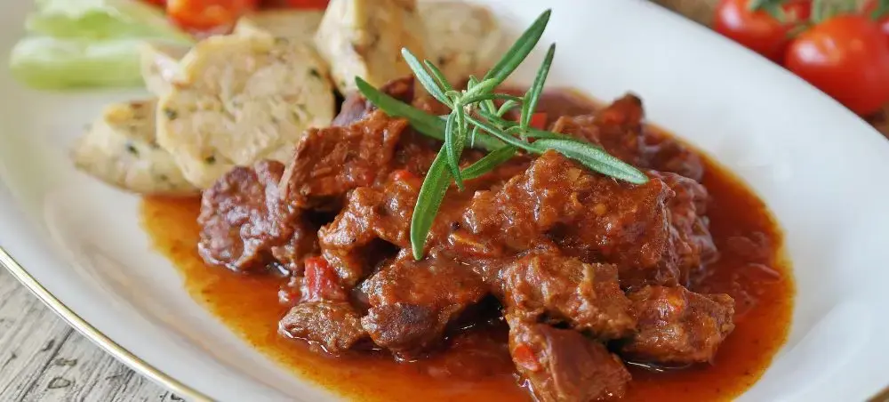 Traditional Hungarian goulash with tender beef in rich paprika sauce, garnished with fresh rosemary