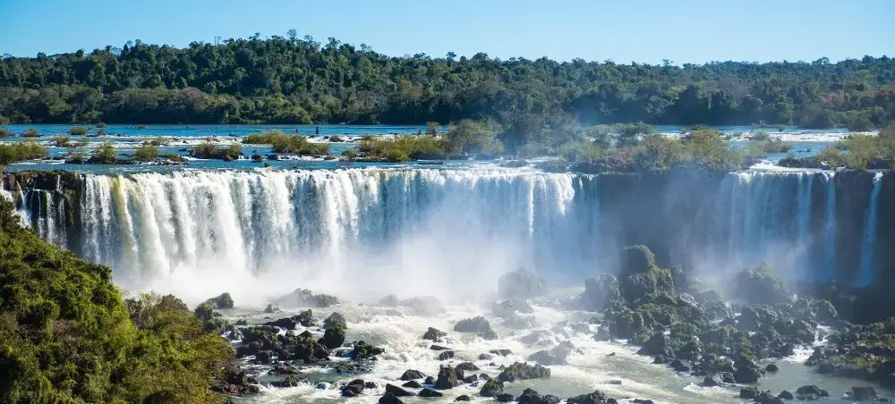 Spectacular Iguazu Falls cascading over cliffs surrounded by lush Brazilian rainforest and mist