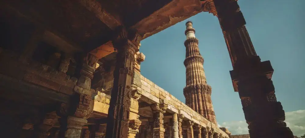 Historic Qutub Minar tower framed by ancient stone arches in Delhi, showcasing India's architectural heritage