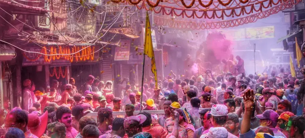 Vibrant Holi festival celebration in India with crowds throwing colorful powder in traditional street