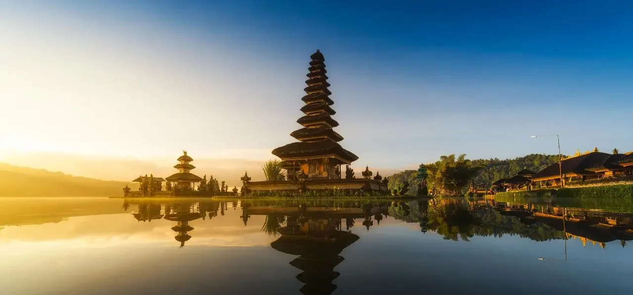 Iconic Balinese temple pagoda reflecting in serene lake waters at golden sunrise in Indonesia