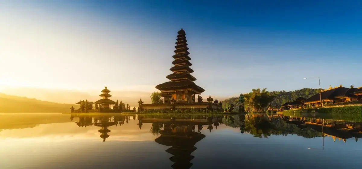 Iconic Balinese temple pagoda reflecting in tranquil lake waters at golden sunrise in Indonesia