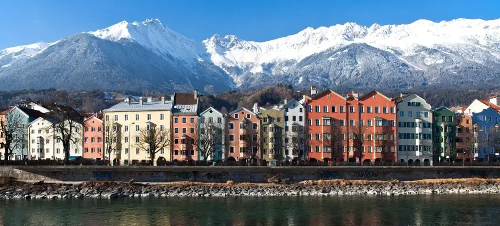 Colorful historic buildings line the Inn River with snow-capped Austrian Alps towering behind Innsbruck