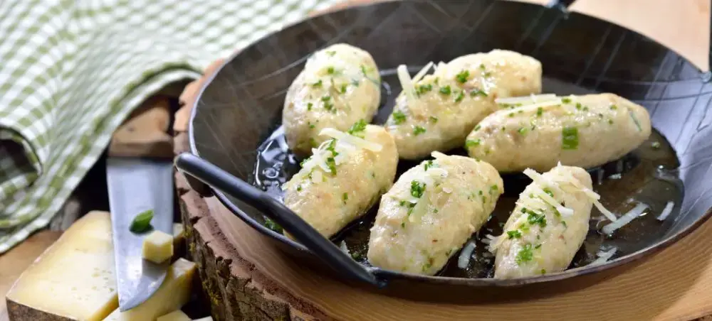 Traditional Austrian dumplings garnished with fresh herbs served in cast iron skillet showcasing Innsbruck culinary heritage