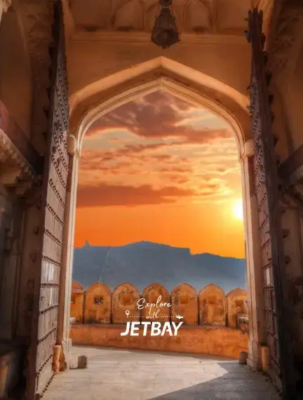 Ornate archway frames golden sunset view over Jaipur's historic Amber Fort courtyard in India