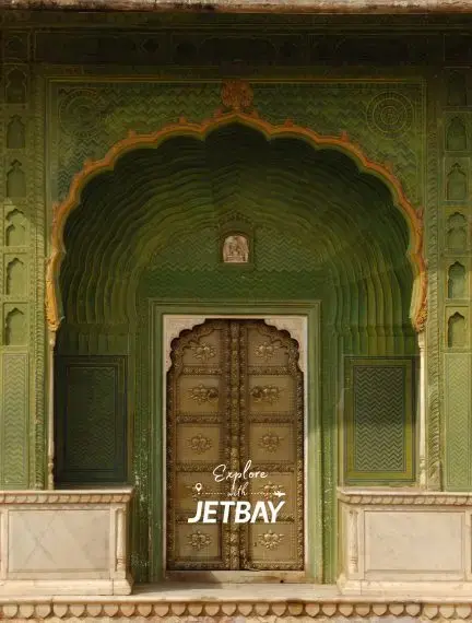 Ornate green Mughal archway with intricate carvings leading to wooden doors in Jaipur's City Palace