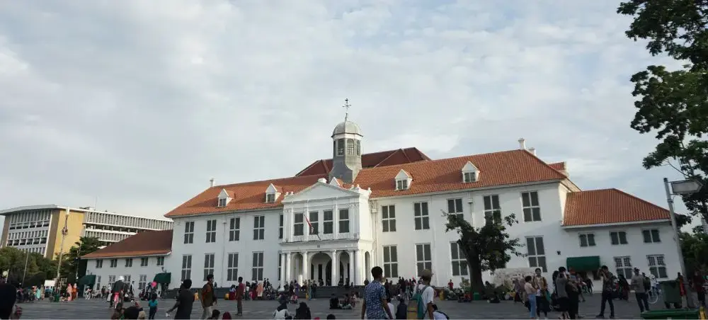 Historic colonial building with red tile roof and clock tower in Jakarta's Old Town square filled with visitors
