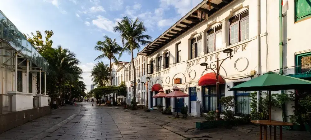 Historic colonial street in Jakarta's old town featuring traditional Indonesian architecture and palm trees
