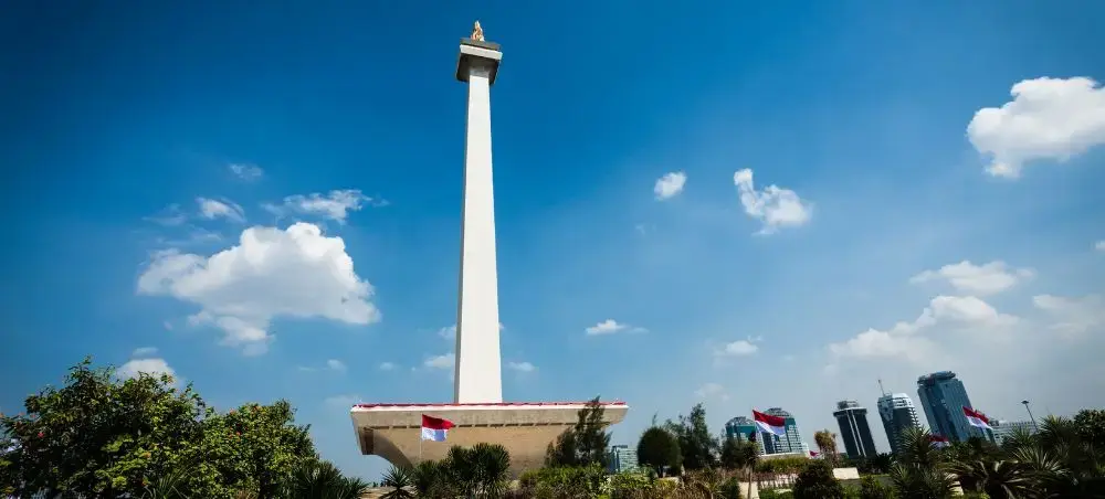 National Monument towering above Jakarta's skyline with modern buildings and lush tropical gardens below
