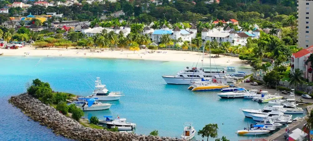 Scenic Caribbean harbor in Jamaica with luxury yachts, pristine beach, and tropical resort villas