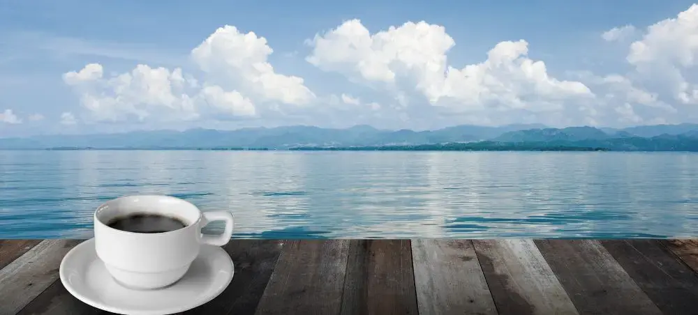 White coffee cup on wooden deck overlooking tranquil Caribbean waters and Jamaica's mountainous coastline