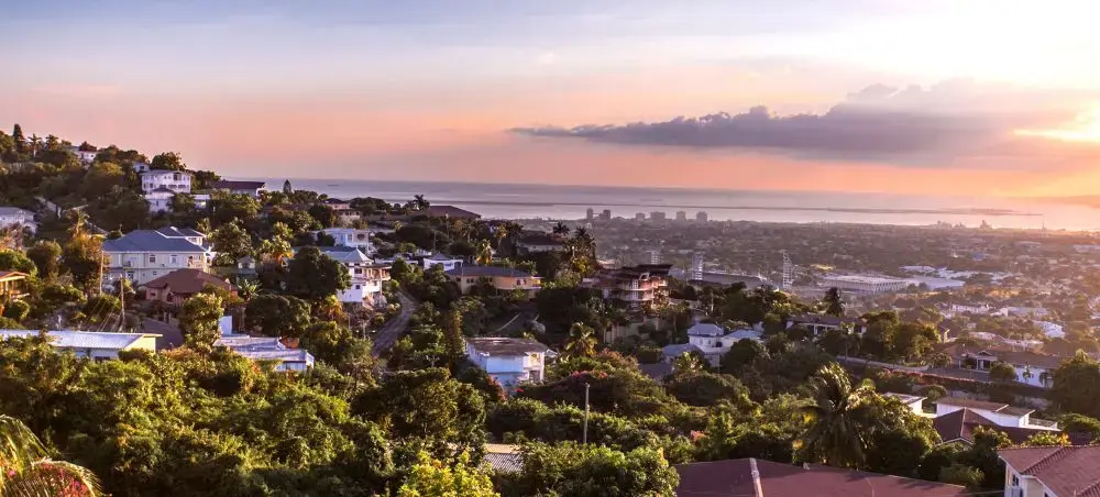 Scenic hillside homes overlooking Jamaica's coastline at sunset with golden light illuminating the tropical landscape