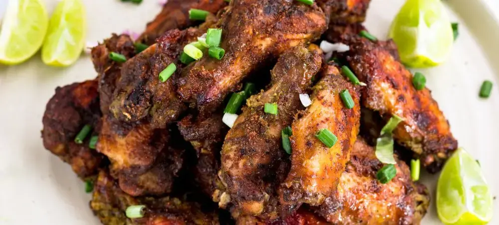 Jerk chicken wings with fresh lime wedges and chopped scallions showcasing authentic Jamaican cuisine