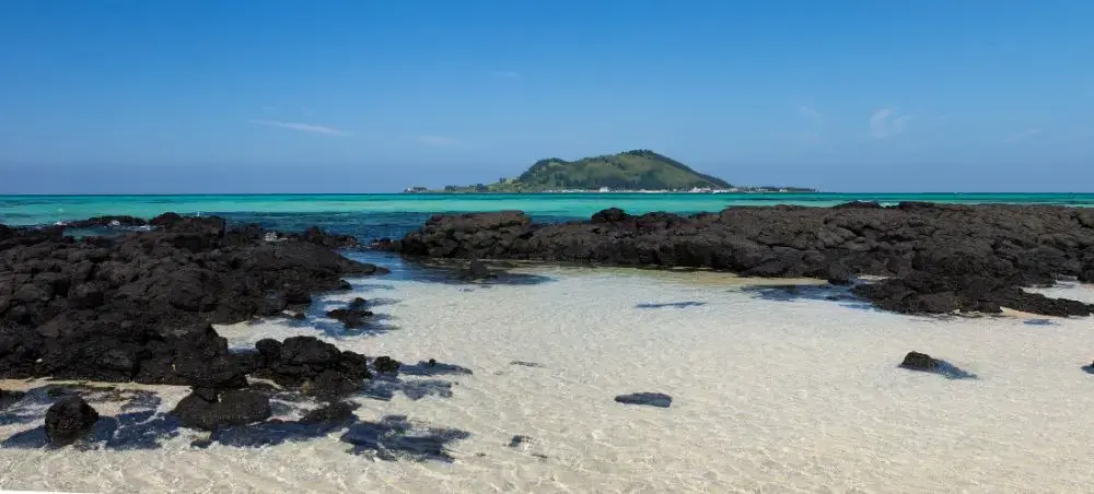 Pristine white sand beach with volcanic rock formations on Jeju Island, showcasing crystal clear turquoise waters
