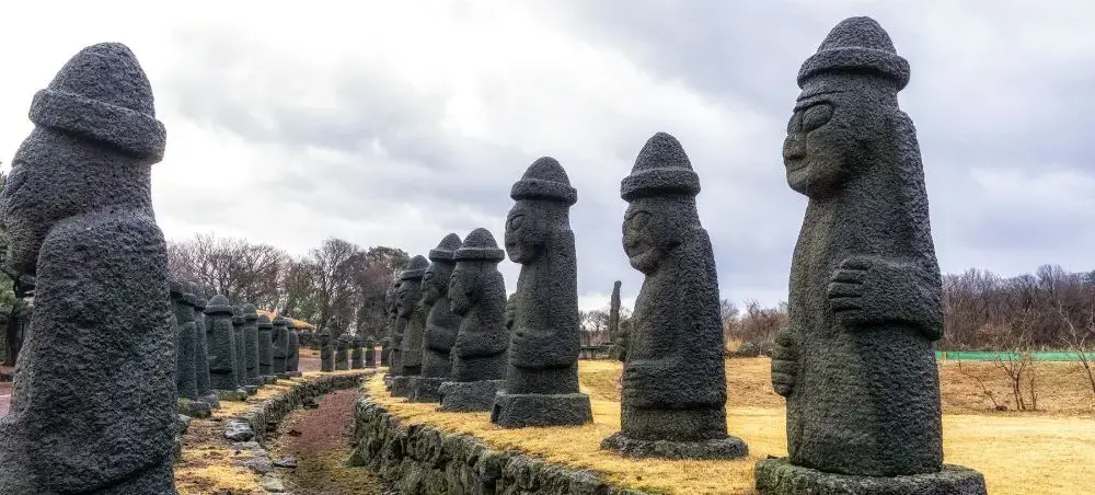 Ancient stone statues called Dol Hareubang standing in rows across golden grassland on Jeju Island, South Korea