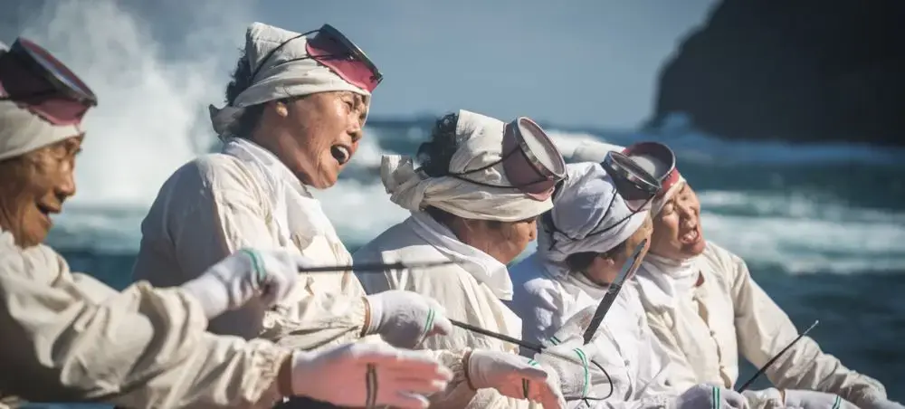 Traditional Jeju Island fishermen in white clothing and headbands working together on their boat near the coast