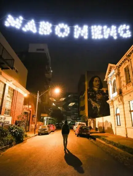Illuminated welcome sign lights up Johannesburg street at night with historic buildings and vibrant murals