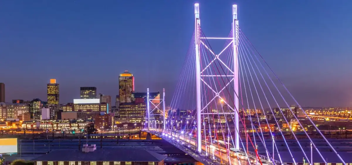 Johannesburg skyline at dusk featuring illuminated Nelson Mandela Bridge and downtown skyscrapers