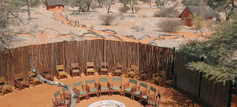 Luxury safari lodge amphitheater with wooden chairs arranged around fire pit in Kenya's red desert landscape