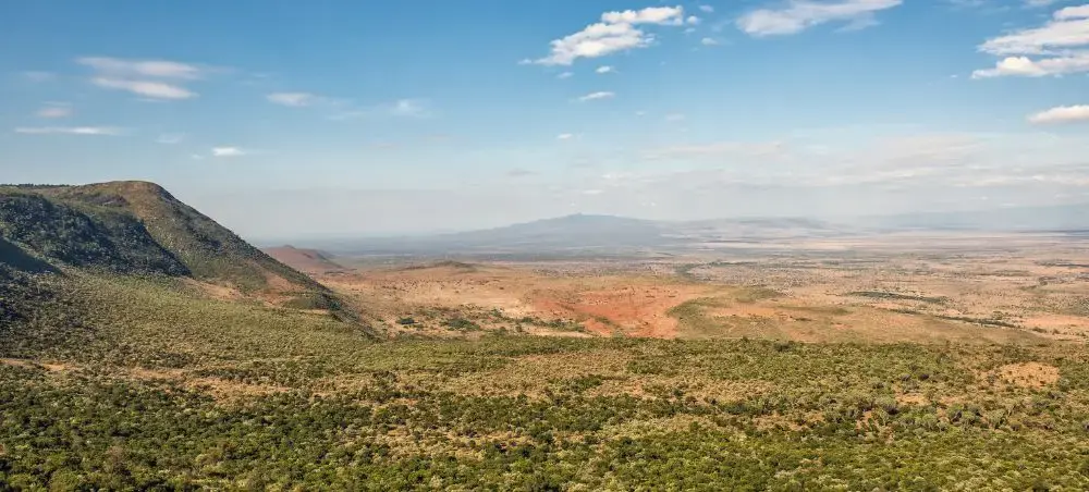 Expansive Kenyan savanna landscape with rolling hills and acacia trees under blue skies perfect for safari