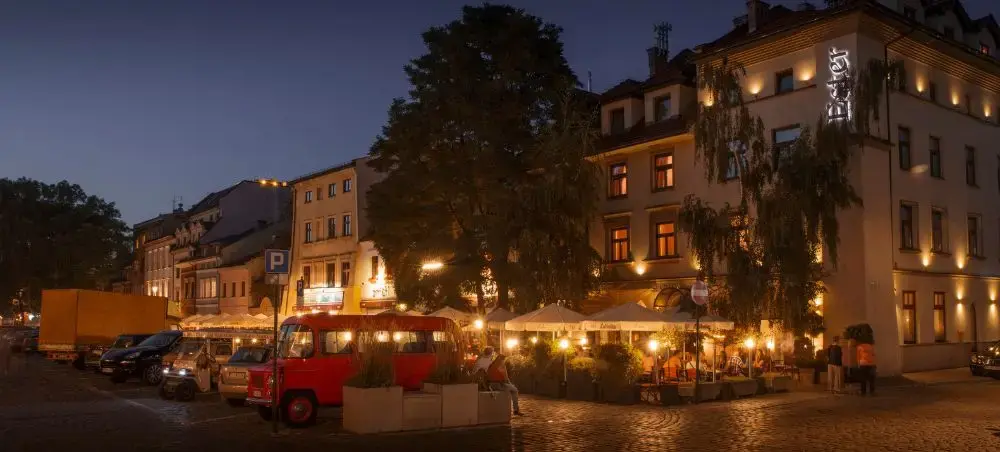 Charming cobblestone square in Krakow's historic district illuminated at twilight with outdoor cafes