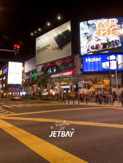Vibrant nighttime street scene in Kuala Lumpur with illuminated billboards and bustling pedestrian activity