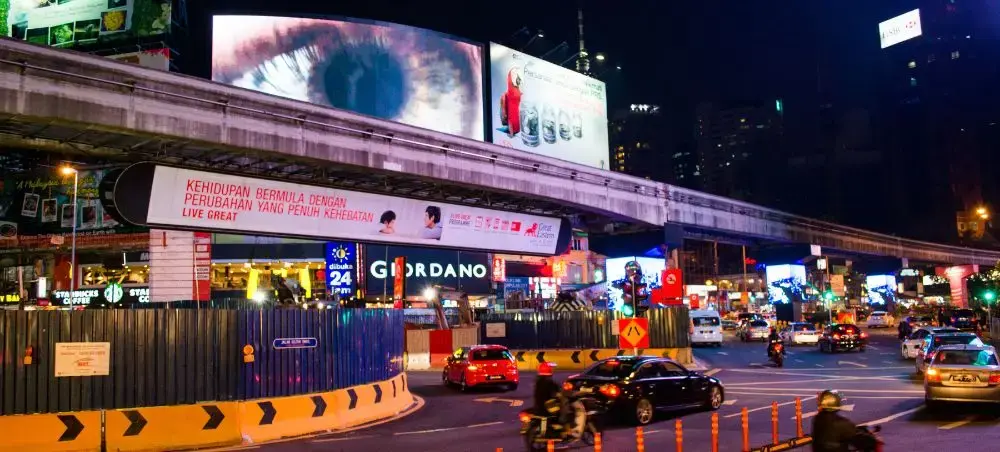 Bustling nighttime street scene in Kuala Lumpur with illuminated billboards and heavy traffic flow