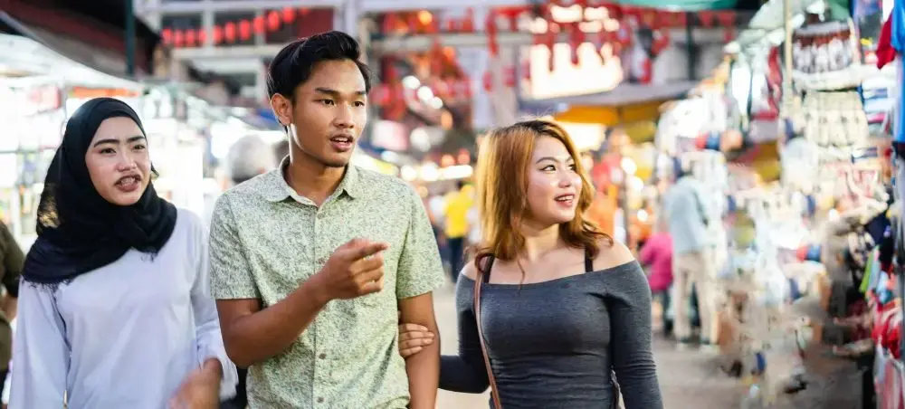 Three friends exploring vibrant Kuala Lumpur street market with colorful stalls and traditional goods