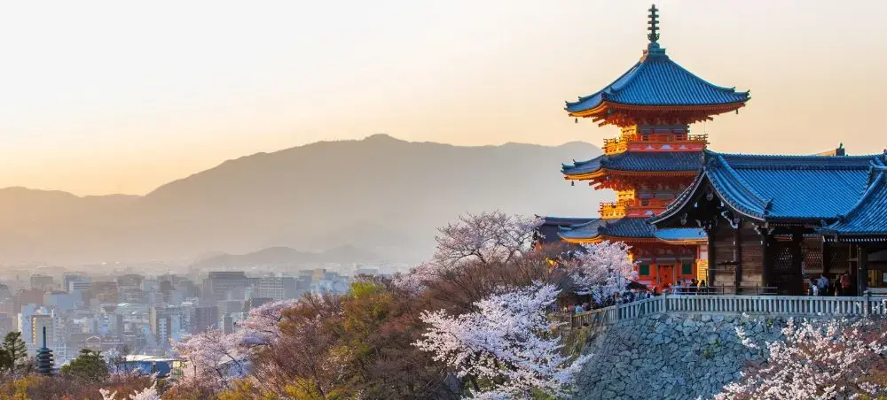 Traditional Japanese pagoda temple overlooking Kyoto cityscape with cherry blossoms at golden hour sunset