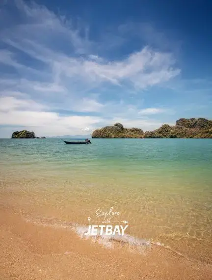 Pristine Langkawi beach with turquoise waters, traditional boat, and lush tropical islands under blue sky