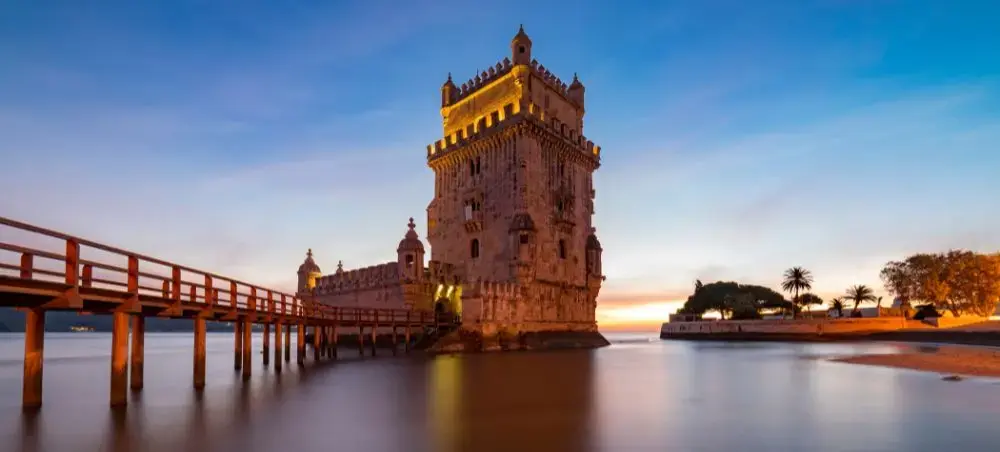 Historic Belém Tower fortress illuminated at sunset with wooden walkway over Tagus River in Lisbon Portugal