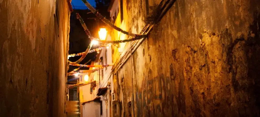 Narrow cobblestone alley in historic Lisbon illuminated by warm street lamps at twilight