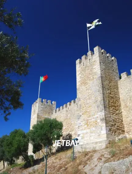Historic Portuguese castle with medieval stone towers and Portuguese flag under brilliant blue sky in Lisbon