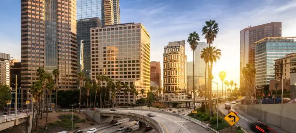 Downtown Los Angeles skyline at golden hour with palm trees and busy freeway showcasing luxury travel destination
