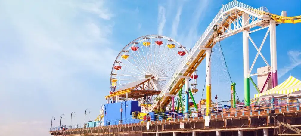 Santa Monica Pier amusement park with colorful Ferris wheel and roller coaster against blue sky in Los Angeles