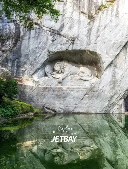 Lion Monument carved into sandstone cliff reflects in tranquil pond, iconic Lucerne landmark for luxury travelers