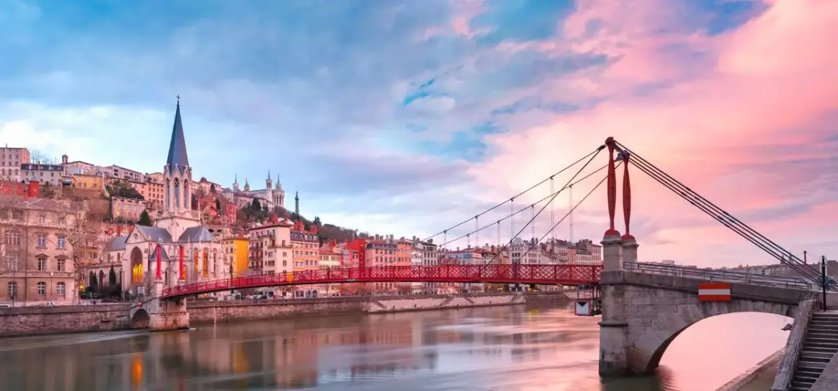 Lyon's historic Passerelle du Palais de Justice bridge spans the Saône River at sunset with colorful buildings