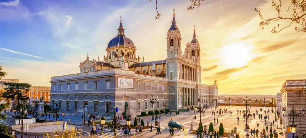 Almudena Cathedral's neoclassical facade and twin towers dominate Madrid's historic plaza at golden hour