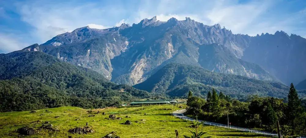 Dramatic Mount Kinabalu peak towering over lush green valleys and winding roads in Malaysian Borneo